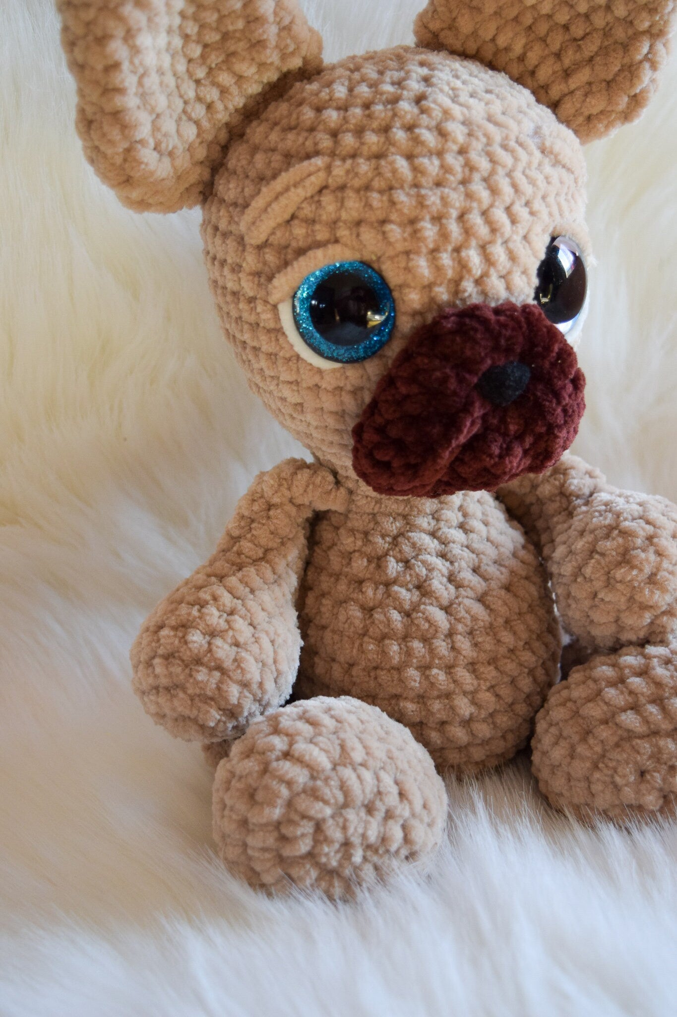 Crocheted dog toy with blue eyes and brown nose on a white surface