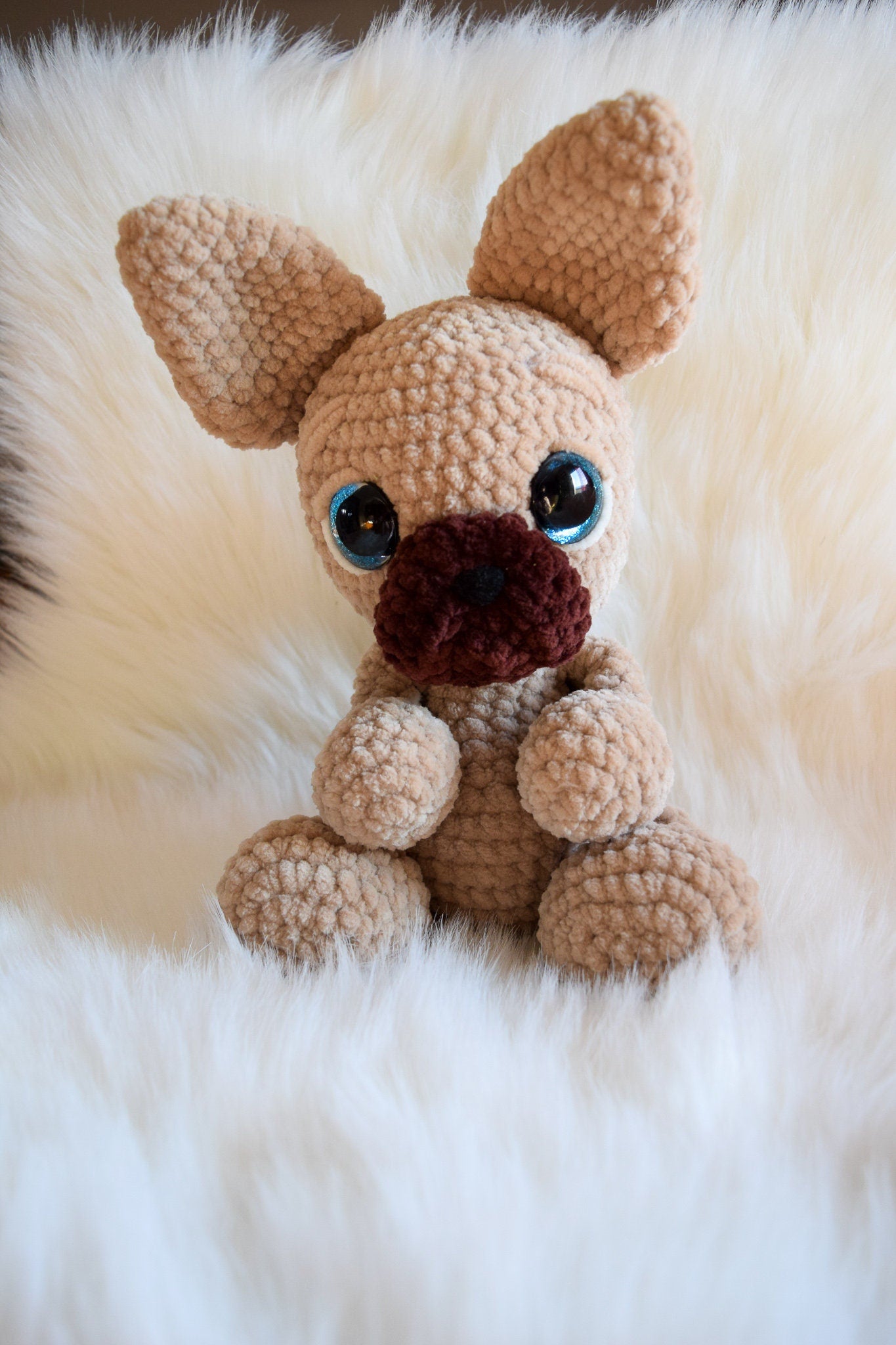 Crocheted dog toy with black eyes and brown nose on a fluffy white surface